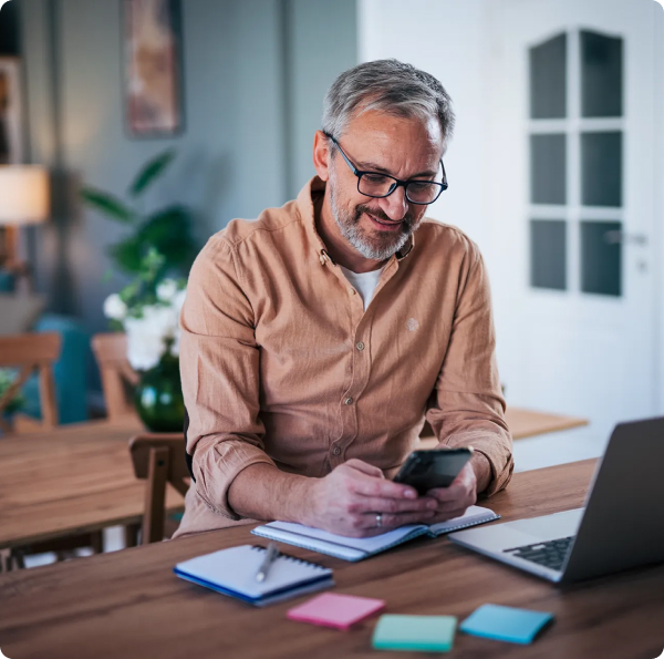 A man sitting at his desk, holding a mobile phone at a desk